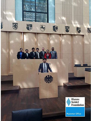 Mr. Achim Munz with 6 Delegates in the background, observing one of the Delegates at the speaker’s desk of the ‘Upper House’ (German Bundesrat). In the upper background some emblems from German States can be spotted.